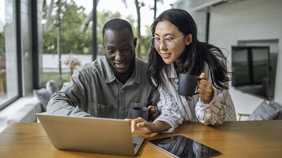 A woman and a man engage in focused discussion over a digital tablet and laptop