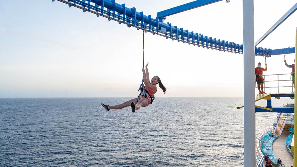 Woman riding a zip line over the ocean on a cruise ship