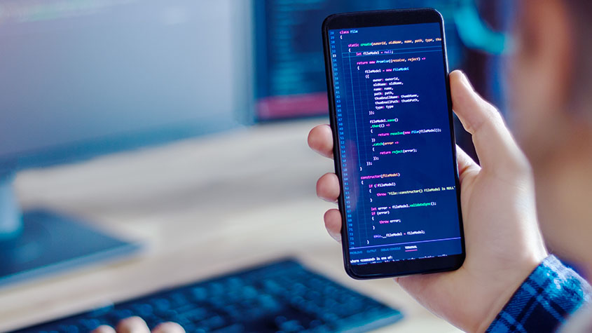 A person holding a mobile phone with development code symbolizing the use of IP for mobile apps development