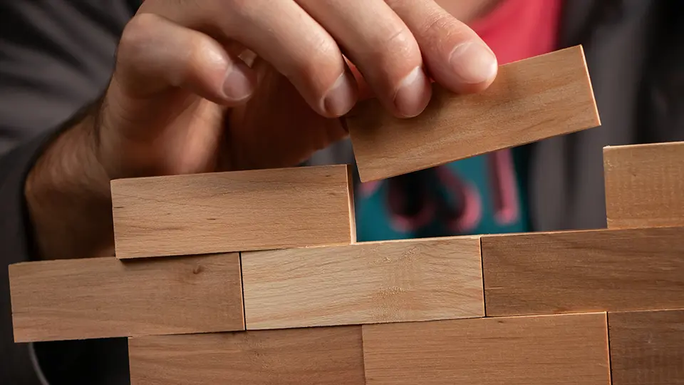 Des mains construisant un petit mur avec des blocs de bois